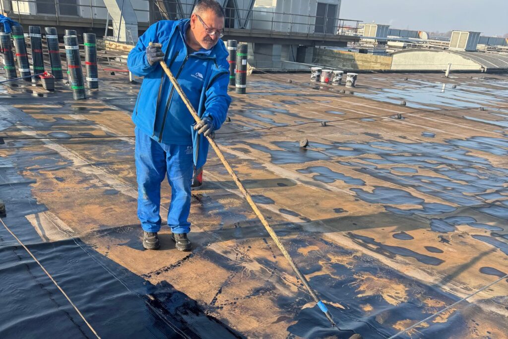 Nostro artigiano specializzato applica primer bituminoso a mano per preparare il rifacimento del tetto.